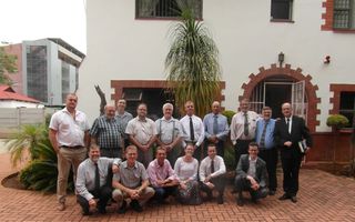 Team van mensen voor een tuin met tropische planten en een huis met een poort. 