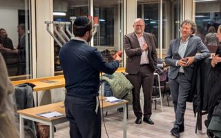 Drie mannen in pak rond een tafel met daarop een negenarmige kandelaar.