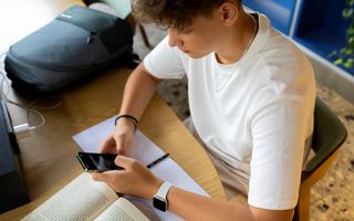 Jongen maakt huiswerk en gebruikt daarbij via zijn telefoon  AI.