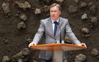 Van Dijk in grijs pak en met blauwe stropdas achter het spreekgestoelte in de plenaire zaal van de Tweede Kamer.