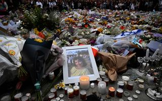 Ingelijste foto van meisje ligt naast grote hoeveelheid kaarsjes en bloemen op straat.