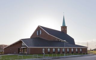 Buitenkant van stenen kerkgebouw met donker dak en toren met groene spits.
