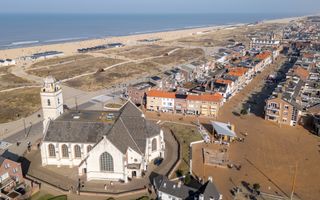 Op de voorgrond een witte kerk, een plein en winkelstraat en daarachter duinen, het strand en de zee.
