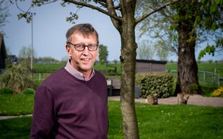 Man in paarse trui staat in een tuin. 