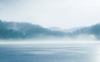 Een meertje tussen de heuvels, met een nevel boven het wateroppervlak.
