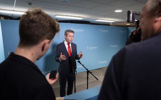 Man in pak staat tegenover journalisten van wie er een aantal op de rug is gefotografeerd.