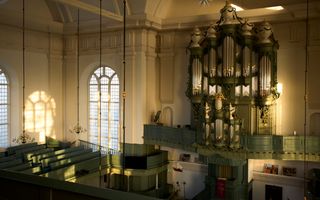 Interieur van de kerk, met een rijkversierd, oud orgel. Eronder de preekstoel, links hoge ramen.