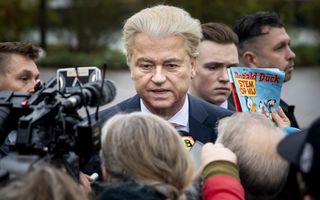 Wilders tussen journalisten en beveiligers.  Iemand houdt een Donald Duck omhoog met daarop de tekst: Stem op mij.
