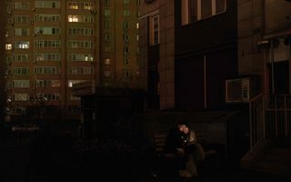 Twee mensen zitten op een bankje in het donker en kijken op een telefoon. 