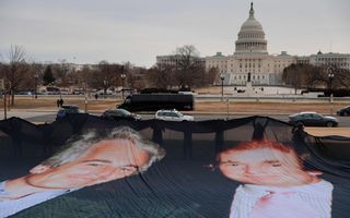 Mensen houden voor een statig wit gebouw een spandoek omhoog met de afbeelding van twee mannen. 