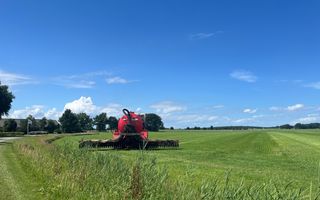 Een rode machine rijdt bij stralend weer mest uit over een weiland.