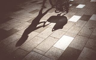 Silhouet op straatstenen van een persoon achter een kinderwagen.