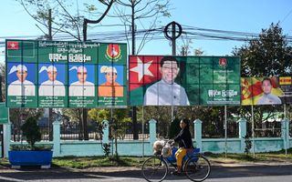 Vrouw fietst over een asfaltweg, waarlangs metershoge borden staan met foto’s van verkiezingskandidaten. 