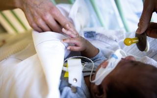 Een kindje ligt op de intensive care. Een verpleegkundige houdt een speen vast. 