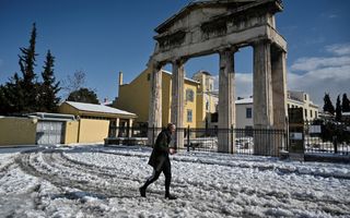 Een man loopt door de sneeuw voor de restanten van een oud Grieks bouwwerk met pilaren.