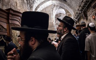 Mannen in zwart pak met hoed op staan te bidden.