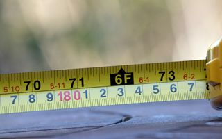 een stukje van een rolmaat, met aan de bovenkant de Amerikaanse en onderaan de metrieke maatverdeling