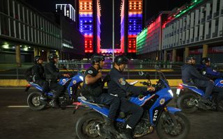 Mannen in donkerblauwe uniformen rijden op motoren door een stad.