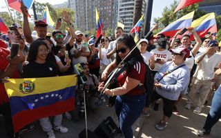 Mensen luisteren op straat naar muzikant, terwijl ze met rood-geel-blauwe vlaggen zwaaien.