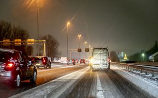 Autosnelweg in de schemer. Een witte bus rijd rijdt over deels besneeuwd asfalt.
