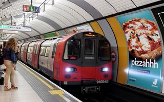 Rood treinstel van de metro staat naast een metershoge reclame met daarop een pizza met gesmolten kaas en de tekst: „pizzahhh”