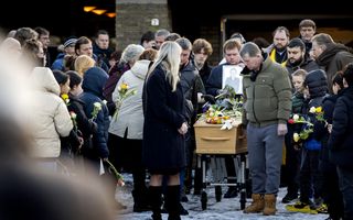 Rouwstoet van verschillende mensen naast een houten kist.