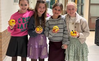 Vier meiden van een jaar of dertien, die elk een zelfgemaakte emoji van klei in hun hand hebben. 