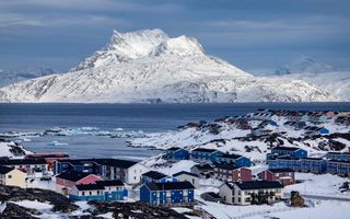 Beeld van huizen in een besneeuwd landschap aan zee, met besneeuwde bergtoppen op de achtergrond.