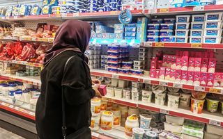 Vrouw met rode hoofddoek staat voor een schap met etenswaren.