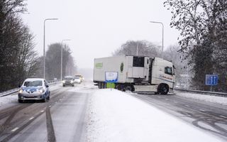 Een snelweg met daarop sneeuw. Een vrachtwagen staat geschaard over de weg.  