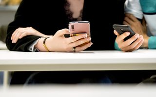 Meisje in een schoolbank zit met telefoon in de hand.