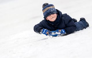 Een jongetje met een muts op en dik aangekleed gaat met een sleetje van een helling.