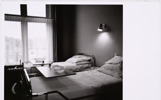 Zwart-witfoto van twee strak opgemaakte ziekenhuisbedden in een kamer.