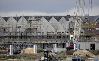 Rijtjeshuizen in aanbouw met op de voorgrond een shovel en een hijskraan.