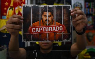 Man heeft met twee handen een foto vast met daarop een boos kijkende man achter tralies en de tekst „Capturado”.