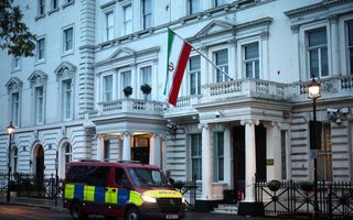 Voor een monumentaal wit pand in Londen staat een politiebusje. Aan het pand hangt een Iraanse vlag: groen, wit, rood.