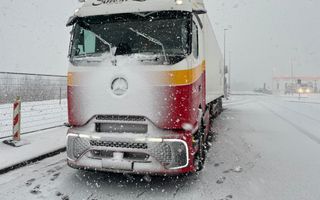 Vrachtwagen in de sneeuw met op de achtergrond een tankstation.