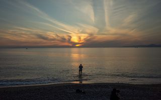 Een man staat in het water van de zee bij een ondergaande zon.