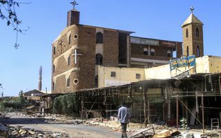 Een man loopt langs een hoog stenen gebouw met daarop meerdere kruizen. 