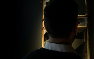 Silhouet van een man met donker haar. Op de achtergrond een kapotgeschoten raam.