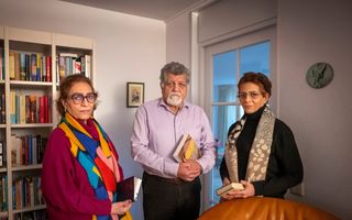 Twee vrouwen en een man staan voor een boekenkast. Zelf hebben ze een boek in het Farsi vast.
