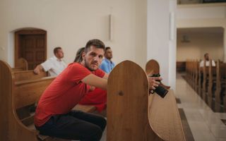 Man in rood shirt zit in een kerkbank. Hij kijkt opzij.