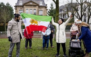 Man in grijze jas houdt met een vrouw die haar handen in de lucht steekt, een Iraanse vlag vast in de kleuren groen-wit-rood.