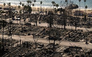 Puinhopen na een brand. Op de achtergrond palmbomen, strand en zee.