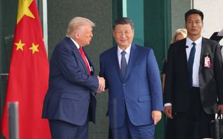 Twee mannen gekleed in blauw pak schudden elkaar de hand. Links is een rode vlag te zien met daarop witte sterren. 