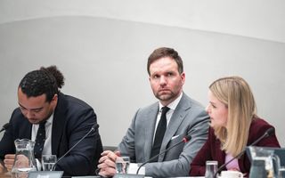 Twee mannen in pak en een vrouw zitten naast elkaar achter een tafel met daarop microfoons en naambordjes, in een commissiezaal van de Tweede Kamer.
