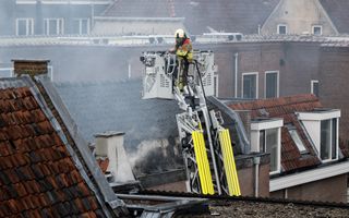 Een hoogwerker met een brandweerman erop boven een huis met veel rook.