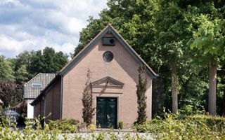 Stenen kerkgebouw met puntdak in bosrijke omgeving.