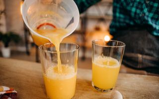 Iemand vult een glas met versgeperst sinaasappelsap. Ernaast staat nog een glas halfvol sap.