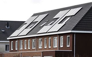Een rij woningen met bakstenen muur en schuin dak met daarop zonnepanelen.